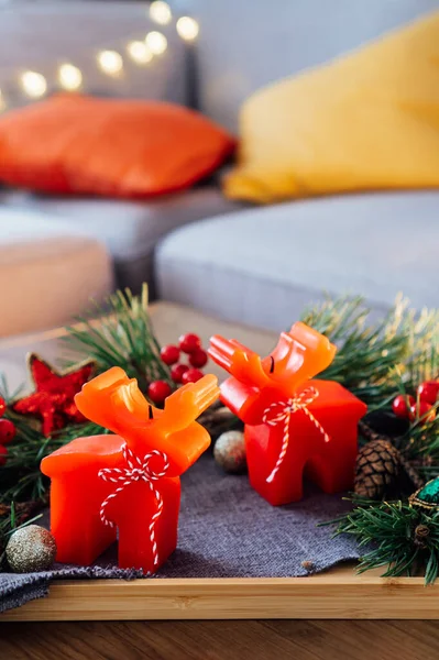 Hygge ev dekorasyonu için Noel kompozisyonu. Geyik şekilli kırmızı mumlar, taze yeşil çam dalları ve oturma odasındaki sehpanın üstündeki sehpanın üzerindeki şenlikli Xmas dekoru. Dikey. Seçici odak