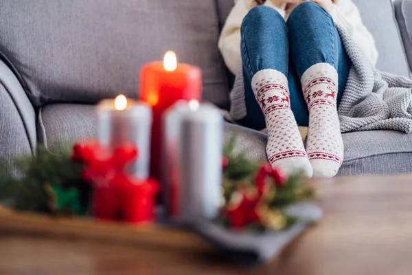 Female feet in xmas woolen socks and cozy Christmas mood candles composition for hygge home on the coffee table. Interior and home coziness concept. Winter and Christmas holidays. Selective focus