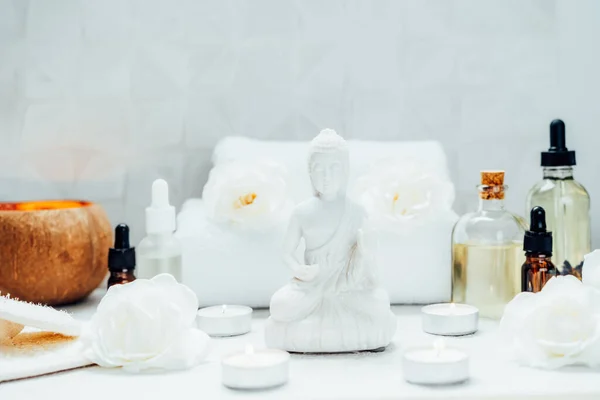 Spa and wellness massage kit and White Buddha statue. Concept of Asian relaxing spa procedure with essential oils. Alternative medicine and body care. Selective focus. copy space