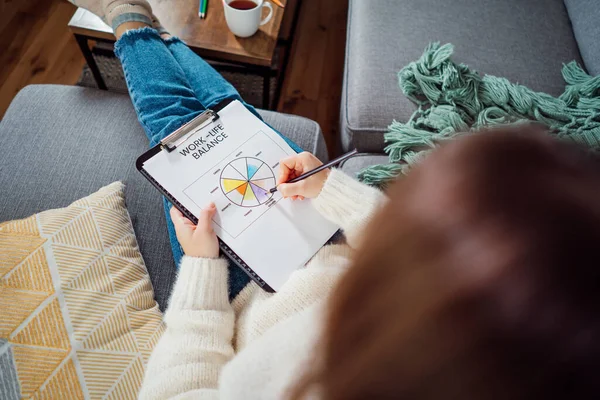Top view relaxed young woman drawing work-life balance wheel sitting on the sofa at home. Self-reflection and life planning. Coaching tools. Finding Balance in Your Life. Selective focus