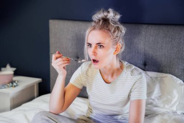 Şok olmuş, stresli, şaşırmış, dondurma yiyen, elinde uzaktan kumandayla yatakta televizyon izleyen bir kadın. Korkunç bir korku filmi ya da korkunç bir haber, gözlerinde korku, aşırı yeme, olumsuz duyguların engellenmesi..