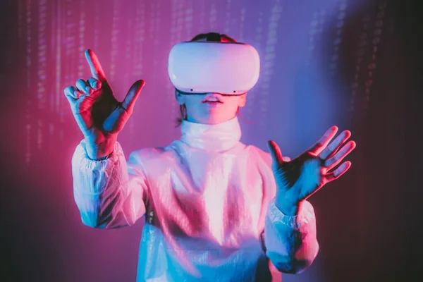 Metaverse concept. Selective Focus on Womans hands in holographic clothes and vr glasses on matrix code background. Virtual reality headset, trying to touch something with hand in pink blue colors.