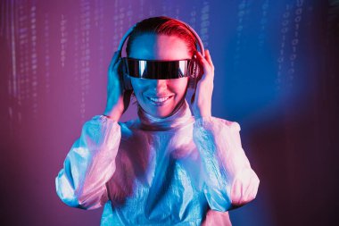 Fütürist güneş gözlüklü, pembe ve mavi ışıklı kulaklıklı gülümseyen bir kadının portresi. Müzik aşığı. Sessiz disko. Matris kod arka planında bir kadın. Geleceğin Partisi.