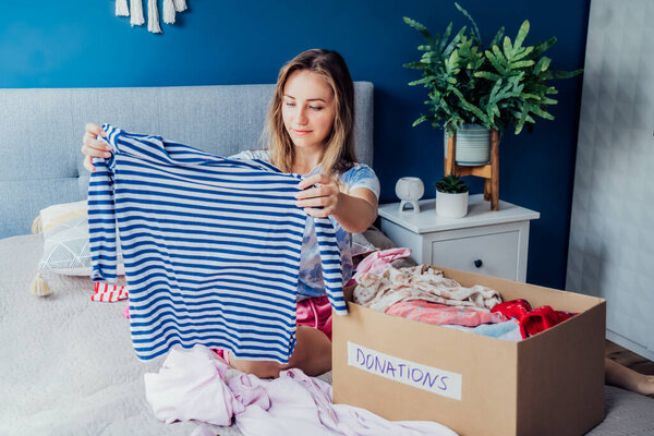 Woman selecting clothes from her wardrobe for donating to a Charity shop. Decluttering, Sorting clothes and Cleaning Up. Reuse, second-hand concept. Conscious consumer, sustainable lifestyle.