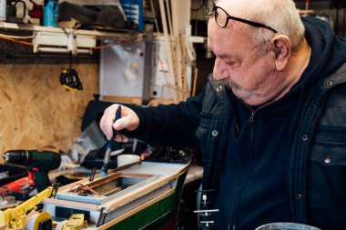 Kıdemli, emekli, garajında farklı malzemelerle el sanatları yapan bir gemi modeli. Emekli yaşlı adam tekne boyama kısmı. Aktif emeklilik yaşam tarzı, hobi. Seçici odak