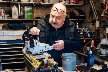 Kıdemli, emekli, garajında farklı malzemelerle el sanatları yapan bir gemi modeli. Emekli yaşlı adam tekne boyama kısmı. Aktif emeklilik yaşam tarzı, hobi. Seçici odak