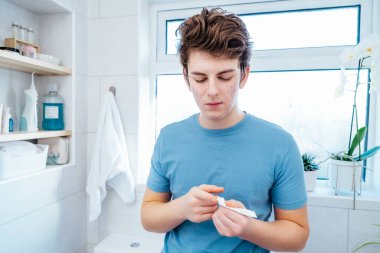 Akne sorunu olan konsantre beyaz çocuk evde cildine dikkat et. Aynaya bakıyor ve banyoda yüzüne krem sürüyor. Her gün ergen cilt bakımı