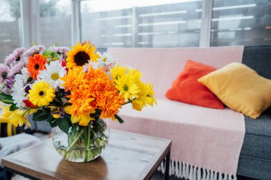Sehpanın üzerinde, kanepe kanepesi ve parlak yastıklı modern rahat konservatuar odasının arka planına sahip çok renkli çeşitli çiçek buketleri olan vazo. İç kısımda taze çiçekler.