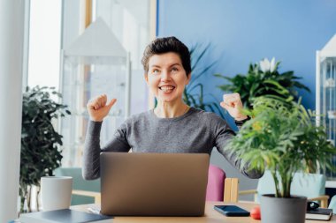 Heyecanlı, mutlu, orta yaşlı, tarafsız, mutlu, mutlu, mutlu, mutlu bir kadın. Kazanan, online olarak seviniyor. Yeni bir iş fırsatı yakaladı, hevesli bir kız, evet hareketi yapıyor.