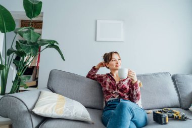 Mutlu bir şekilde gülümseyen genç bir kadın evinin duvarına kendi resmini astıktan sonra kahve fincanıyla rahatlıyor. Oda temizliği işi. Kendini tamir ediyor. DIY, cinsiyet eşitliği kavramı.