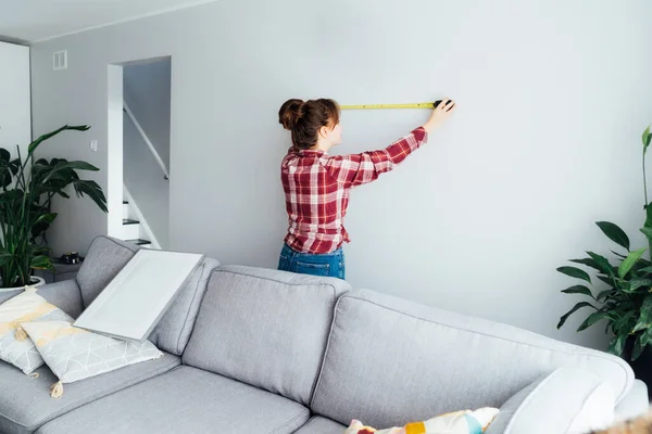 壁に測定テープを貼って測定をしている若い女性 女の子は家に壁に絵を置きたいと思っている 家事労働 自分で修理してる Diy 仕事の概念における男女共同参画 — ストック写真