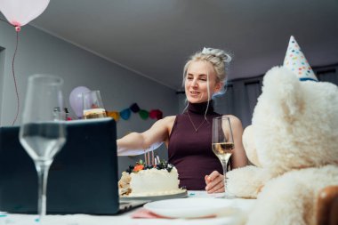 Parti şapkalı genç kadın şampanya içip pasta yiyor, arkadaşlarıyla online doğum günü partisi veriyor. Kız konuşması, görüntülü konuşma, yaşam tarzı blogu, webcam görüntüsü. Evde kal, karantina konsepti