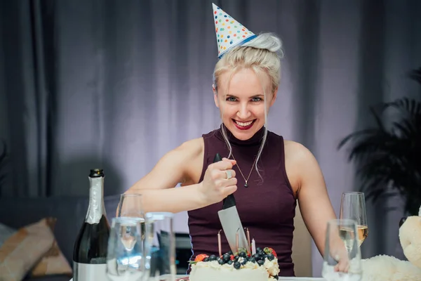 stock image Attractive crazy laughing birthday woman with bread-knife planning to cut her birthday cake while celebrating birthday at home alone. Selective focus.