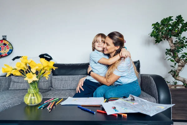 笑顔の息子は 自宅の家族の週末の間に彼の幸せな母親を抱きしめて母と息子はリビングルームで色鉛筆やマーカーで描画します 子供の創造性の概念 選択的焦点 — ストック写真