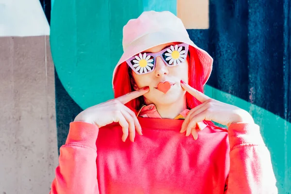 Woman with pink hair, bucket hat in sunglasses with flowers stickers and heart-shaped sticker on the lips. Makeup, cosmetics, artificial beauty, fashion doll concept. Vanilla Girl. Candy color design