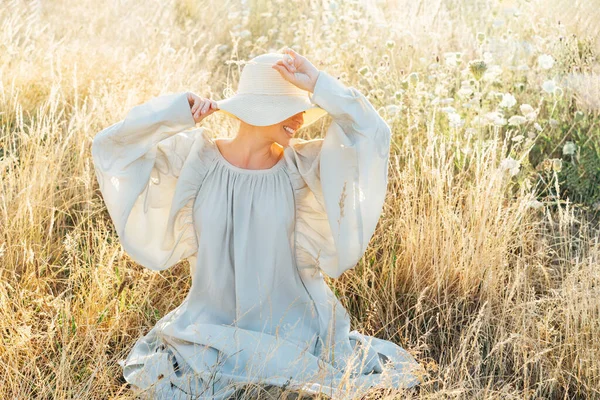 薄い風通しの良いドレスと草の刃を保持し 高草の牧草地で日没時に瞬間を楽しむわら帽子の公開認識できない女性 自然の中で夏の夜 落ち着いて調和を — ストック写真