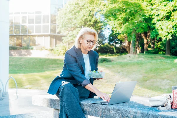 Mulher Negócios Meia Idade Almoçando Sentada Com Laptop Banco Parque — Fotografia de Stock