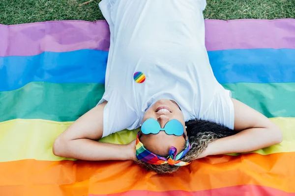 stock image Top view smiling mixed-race woman lying on a rainbow flag. A young lesbian activist with symbol of social movement Lgbtq. Fight for equality, freedom and human rights. Celebrating Pride month