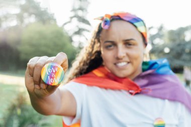 Genç gülümseyen lezbiyen aktivistin elinde LGBTQ gökkuşağı rozeti. Aşk ile yuvarlak rozet aşk mesajıdır. Eşitlik, özgürlük ve insan hakları için savaş. Gurur Ayı 'nı kutluyoruz. Seçici odak