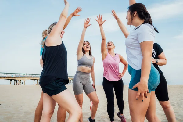 Happy fitness class giving high five after completing workout on beach. Multi aged women motivated after session together, engaged in team building, join hands for shared goal or success at training.