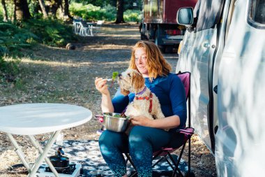 Şaşırmış orta yaşlı bir kadın, köpek yavrusu köpeğiyle orman kampındaki karavanın dışında vejetaryen salatası kokluyor öğle yemeği sırasında. En iyi arkadaşım. Özgür yaşam tarzının, tatilin tadını çıkarıyorum. Hayvanlarla seyahat et.