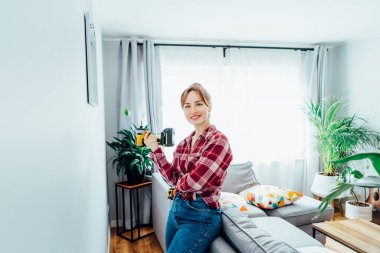 Evinin duvarına bir resim astıktan sonra elinde elektrikli tornavidayla mutlu bir şekilde gülümseyen genç kadın. Oda temizliği işi. Kendini tamir ediyor. Ev dekorasyonu. DIY kavramı.