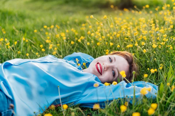 黄色の花と緑の芝生の芝生の上に横たわって青いブラウスで幸せな若い女性の笑顔の肖像画 女性は日没時に屋外でリラックスして瞬間をお楽しみください 精神衛生 アレルギーの概念なし — ストック写真