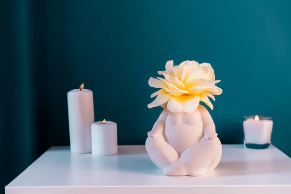 stock image Close up white table with ceramic female body-shaped vase with rose flower, burning candles on turquoise blue wall background. Zen, cozy, meditation female bedroom decor. Self recovery place at home