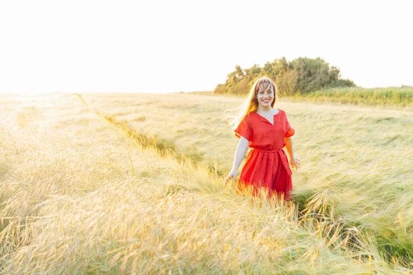 夕日の小麦畑を歩いて赤いドレスを着た若い幸せな女性 自由の息だ 肯定的な感情の生活 心の平和を感じる 精神衛生の練習 自然のリラックス 柔らかい選択的フォーカス — ストック写真