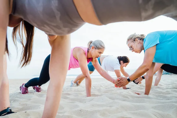 stock image Women of various ages doing fitness workouts in class exercise with coach on beach. Ladies doing paired plank exercises and high-fiving each other. Sport for health and wellbeing. Active lifestyle.