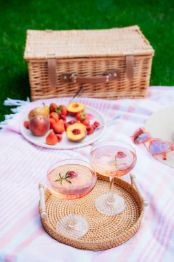 Pink drinks, cocktail with ice, raspberry, rosemary. Two glasses with martini, champagne, cider, lemonade on the blanket with fruit plate, picnic basket. Cozy summer picnic on nature. Selective focus