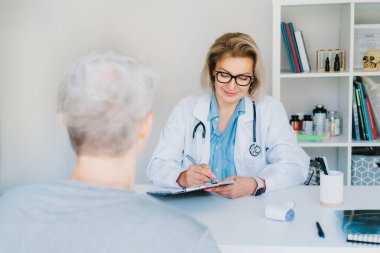 Orta yaşlı, profesyonel bir doktor olan kadın doktor konsültasyonda yaşlı, olgun bir hastaya danışmanlık yapıyor ve sağlık kontrolünde müşteriyle konuşuyor. Yaşlı sağlık hizmetleri konsepti.