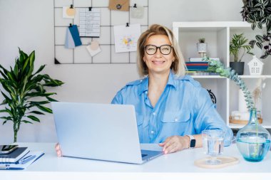 Ofisinde laptopuyla gülümseyen olgun bir iş kadını, kendinden emin orta yaşlı tecrübeli bir bayan profesyonel, kameraya bakan şirketin CEO 'su. Yaratıcı girişimci işletmeyi yönetir