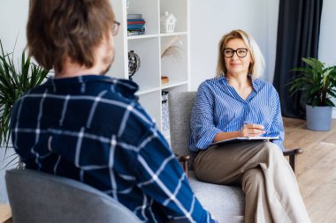 Profesyonel psikoterapi. Ruh sağlığı kliniğinde erkek hastayla seans yapan kadın psikolog, ofisinde randevu sırasında not alıyor. Psikolojik yardım servisi. Depresyon tedavisi