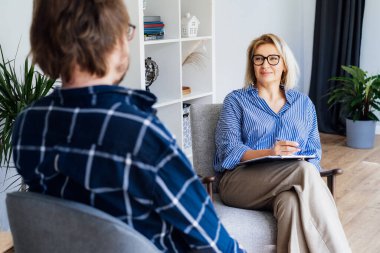 Professional psychotherapy. Female psychologist having session with male patient at mental health clinic, Taking Notes During Appointment In Office. Psychological help service. Treatment of depression clipart