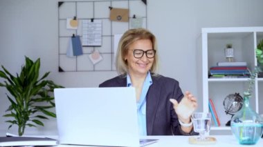 50 'li yaşlarda gülümseyen, olgun bir iş kadınının bilgisayarda görüntülü konuşma yapması. Orta yaşlı, tecrübeli, rahat bir ofiste dizüstü bilgisayarla çalışan bir bayan profesyonel. Uzaktan çalışan kadın girişimci.