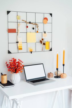 Ev ofis masası, açık dizüstü bilgisayarı, sonbahar renkleri paletli şebeke modülü ve mumlar, çiçekler, balkabakları gibi mevsimsel dekorlar. Sonbahar ilhamı ve samimi bir ruh hali. Hygge ev sonbahar dekoru. Dikey