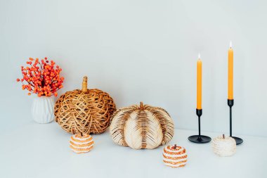 Konforlu sonbahar çevre dostu ev dekorasyonu çeşitli dekoratif hasır balkabakları, yanan mumlar, açık gri arka planlı beyaz masa üzerindeki vazoda mevsimlik çiçekler. Sonbahar Ruh hali ilhamı.