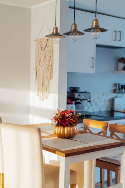 Mutfak tezgahında beyaz, modern mutfak arka planına sahip altın bir kabak vazosundaki parlak yapay çiçeklerden oluşan sonbahar buketi. Şükran Günü ve Cadılar Bayramı için sonbahar ev dekorasyonu. Dikey