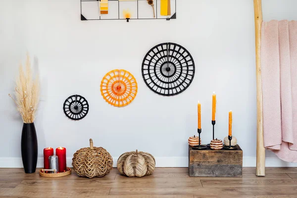 Cozy autumn eco-friendly home interior decor- various decorative wicker pumpkins, burning candles, dried flowers in vase on wooden floor and gray wall background. Autumnal Mood inspiration
