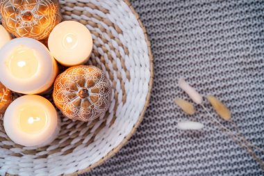 Üst görünüm sonbahar sonbaharı ev dekorasyonu için rahat kompozisyon. Mandalalarla süslenmiş turuncu balkabakları hasır tabakta yanan beyaz mumlar örülmüş gri ekose üzerinde kurutulmuş Pampa otları. Kapat..