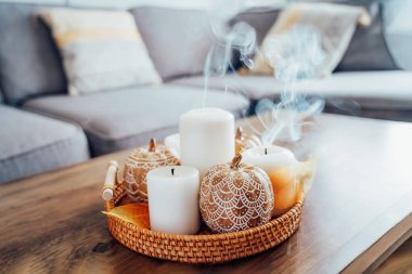 Hygge ev dekoru için sonbahar havası kompozisyonu. Mandalalarla süslenmiş turuncu balkabakları oturma odasındaki sehpanın üstündeki sehpada dumanla süslenmiş beyaz mumlar. Seçici odak