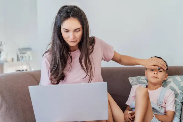 Stressed mother talking with pediatrician doctor during online video chat on pc, worried about her sons health, checking childs temperature by holding hand on kid forehead. Telemedicine, telehealth