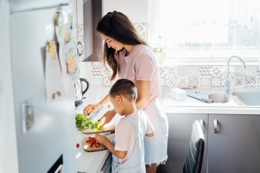 Sevgi dolu genç bir anne, anaokulu çocuğuna evde sağlıklı yemek ya da salata hazırlıyor, modern mutfakta çocukla birlikte yemek pişiren mutlu bir anne, annesiyle yemek hazırlayan bir çocuk..