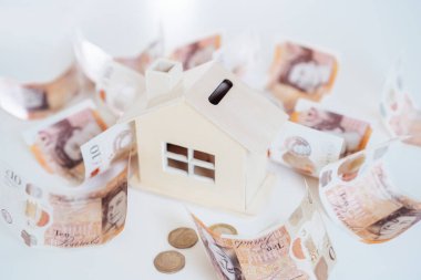 Ahşap Ev modeli, beyaz masada İngiliz parasıyla kumbarası. Konut giderleri ve ödemeler. Gayrimenkul veya gayrimenkul yatırımı. Ev kredisi oranı. Emeklilik kavramı için para biriktiriyorum