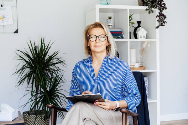 Professional Psychotherapy. Successful female Psychologist Smiling To Camera Sitting On armchair In Office. Mature 50s middle-aged professional portrait of teacher, coach, mentor, therapist, counselor