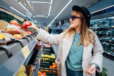 Taze ürünler seçerken süpermarkette taze organik nar alan şık moda gülümseyen kadın. Market alışverişi. Sağlıklı beslenme, vejetaryen ol. Seçici odaklanma. Boşluğu kopyala