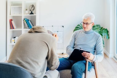 Profesyonel psikoterapi. Ruh sağlığı kliniğinde erkek hastayla seans yapan erkek psikolog ofisinde randevu sırasında not alıyor. Psikolojik yardım servisi. Depresyon tedavisi.