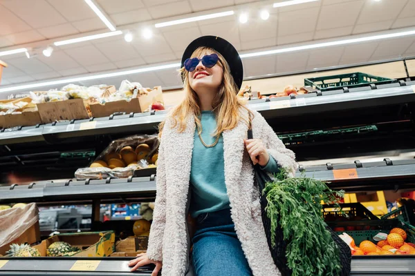 Portrait of Stylish fashion smiling woman in the supermarket store during selecting fresh products. Healthy eating diet, go vegan. Grocery Shopping. Veganuary diet month. Selective focus.