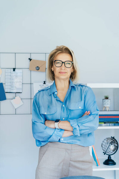 Портрет 50-х годов стильная, уверенная в себе зрелая деловая женщина, директор компании среднего возраста, опытная старшая женщина-профессионал, руководитель команды бизнес-тренеров в современном офисе. Женщина-лидер. Вертикаль.